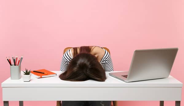 Woman is frustrated by timesheeting, resting head on desk.